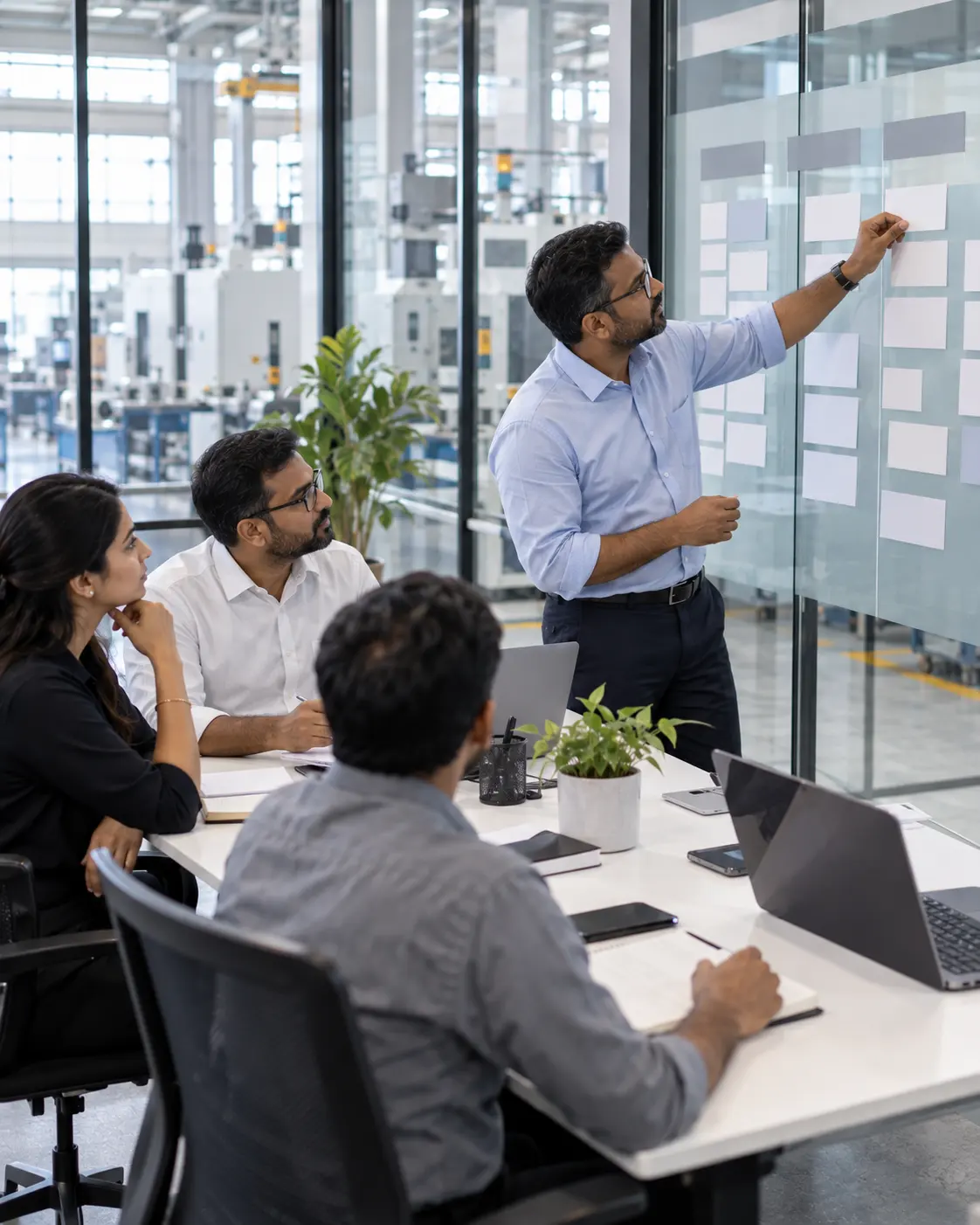 A strategy workshop in a glass walled meeting room beside a factory floor